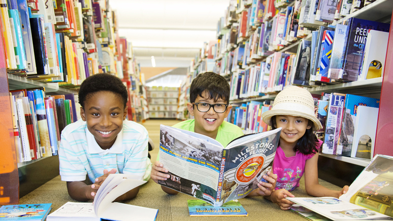 3 kids smiling with books on floor of the library