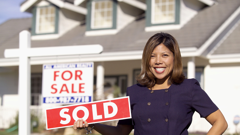 realtor holding sold sign in front of house