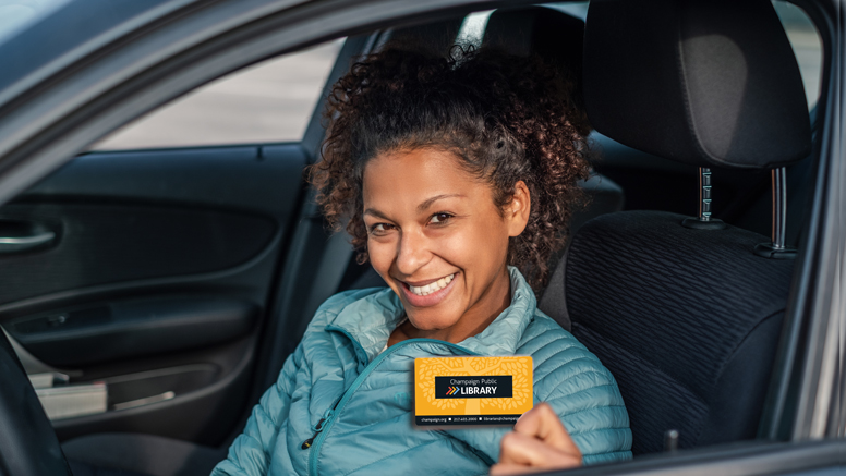 woman holding library card and smiling through car window